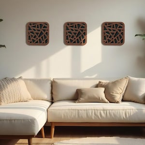 May include: Three square wooden wall art pieces with a geometric design are mounted on a white wall above a cream-colored sectional sofa. The art has a dark interior and a brown frame.
