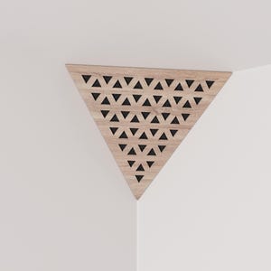 May include: A wooden corner shelf with a triangular shape. The shelf is light brown with a pattern of black triangles cut out across the surface. The shelf is mounted in the corner of a white wall.