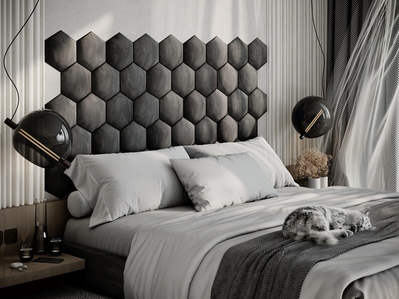 Puede incluir: Un dormitorio moderno con una cama con ropa de cama y almohadas blancas, una manta gris estampada y un cabecero gris compuesto por paneles hexagonales. Un gato duerme en la cama. Dos l&aacute;mparas colgantes negras en forma de globo cuelgan del techo.