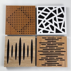 May include: Four square wooden acoustic panels with different designs. One panel is brown with black circular perforations. Another is white with a black geometric pattern. The other two panels have black linear cutouts on wood.