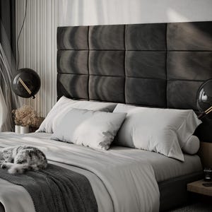 May include: A modern bedroom scene featuring a bed with a dark gray headboard and light gray bedding. Two spherical black pendant lights hang above the bed. A gray and white cat is curled up on the bed. The room has a minimalist design.