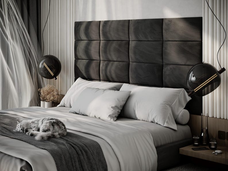 May include: A modern bedroom scene featuring a bed with a dark gray headboard and light gray bedding. Two spherical black pendant lights hang above the bed. A gray and white cat is curled up on the bed. The room has a minimalist design.