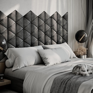 Puede incluir: Un dormitorio moderno con una cama con cabecero gris compuesto por paneles en forma de diamante. La cama está cubierta con ropa de cama blanca y una manta gris estampada. Un gato duerme en la cama. Lámparas colgantes negras.