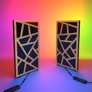 Könnte beinhalten: Zwei rechteckige Holzpaneele mit geometrischem Design. Die Paneele haben einen hellen Holzrahmen, einen dunkelblauen Innenraum und ein Netzwerk aus geometrischen Formen aus hellem Holz. Jedes Paneel hat ein schwarzes Kabel und einen kleinen schwarzen Stecker.