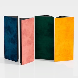 Op de afbeelding: Vier rechthoekige, rechtopstaande objecten met een driehoekige bovenkant. De objecten zijn in tinten blauw, roze, groen en geel. Elk heeft een textuur en een zwarte bovenkant. Ze zijn in een rij gerangschikt tegen een witte achtergrond.