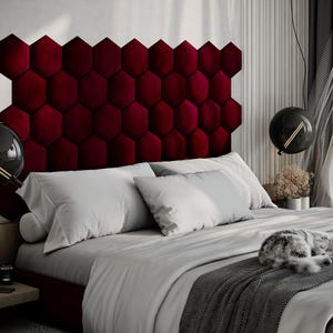 Puede incluir: Un dormitorio moderno con una cama con un cabecero burdeos en forma de hex&aacute;gono. La cama est&aacute; cubierta con ropa de cama blanca y una manta gris. Un gato est&aacute; durmiendo en la cama. L&aacute;mparas negras en forma de globo cuelgan del techo.