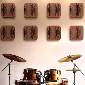 May include: Acoustic treatment panels and a drum set. Eight square wooden panels with vertical black lines are mounted on a wall. Below, a drum set with cymbals and drums in a warm wood finish is visible.