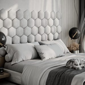 Puede incluir: Un dormitorio moderno con una combinaci&oacute;n de colores gris y blanco. La cama tiene un edred&oacute;n gris, almohadas y una manta estampada. Un gato est&aacute; durmiendo en la cama. El cabecero est&aacute; hecho de paneles hexagonales. Dos l&aacute;mparas colgantes negras.