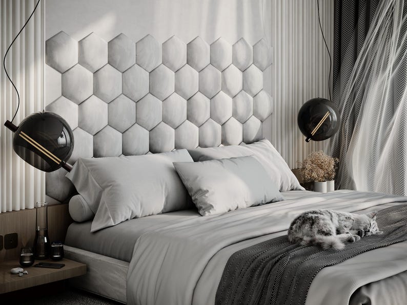 Puede incluir: Un dormitorio moderno con una combinaci&oacute;n de colores gris y blanco. La cama tiene un edred&oacute;n gris, almohadas y una manta estampada. Un gato est&aacute; durmiendo en la cama. El cabecero est&aacute; hecho de paneles hexagonales. Dos l&aacute;mparas colgantes negras.