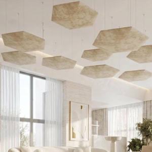 Puede incluir: Un interior moderno con múltiples paneles de techo beige y geométricos suspendidos del techo. La habitación tiene grandes ventanales con cortinas blancas transparentes, un sofá blanco y una obra de arte abstracta enmarcada.
