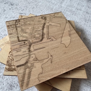 May include: A stack of square wooden coasters with a detailed map of a town etched into the surface. The word "ESTOFT" is visible. The coasters are made of light-colored wood.