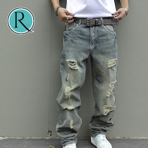 May include: Light blue distressed jeans with multiple rips and tears. The jeans have a relaxed fit and a faded wash. A black studded belt is worn with the jeans. The jeans are part of a casual wear collection.