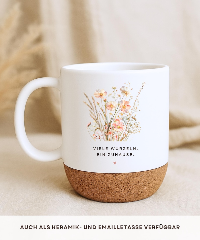May include: White ceramic mug with a cork base. The mug features a floral design with the text "VIELE WURZELN. EIN ZUHAUSE." in black. A small pink heart is below the text. The mug has a white handle.