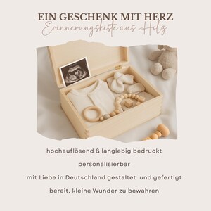 May include: A light-colored wooden keepsake box, open to reveal baby items. Inside are a onesie, booties, a wooden teething ring, and a beaded teether. The box also contains a sonogram photo. Text on the image reads "A gift with heart."
