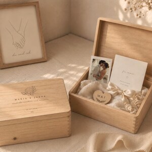 Puede incluir: Dos cajas de madera clara para recuerdos. Una caja est&aacute; cerrada y presenta un grabado de concha, los nombres Maria & Jakub y una fecha. La caja abierta contiene una fotograf&iacute;a de una pareja, una tarjeta con texto, una cinta crema y un coraz&oacute;n.