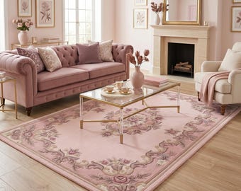 May include: A pink living room with a tufted sofa, armchair, and a patterned rug. A glass coffee table with gold trim sits in front of the sofa. The room is decorated with framed artwork and a fireplace with a gold-framed mirror.