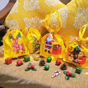 May include: Yellow drawstring gift bags with Christmas-themed designs, including a reindeer, Christmas tree, and Santa Claus. The bags are decorated with gold ribbon and are surrounded by small Christmas ornaments and decorations.