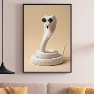 Puede incluir: Una lámina de arte mural enmarcada que muestra una cobra blanca enroscada sobre un fondo beige liso. La serpiente lleva puestas unas gafas de sol pequeñas, redondas y oscuras, y sostiene en la boca un objeto fino y oscuro similar a un cigarrillo.