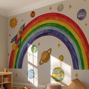 May include: A wall decal set featuring a large watercolor rainbow, a rocket ship, a smiling sun, and various planets with rings and faces. The design includes small yellow stars scattered across the wall, creating a space-themed mural.