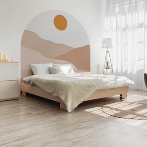 May include: A light wood bed frame with a white duvet and a fluffy, cream-coloured blanket. The headboard features a mural of a desert landscape with a sun. A white dresser and a floor lamp are also visible.