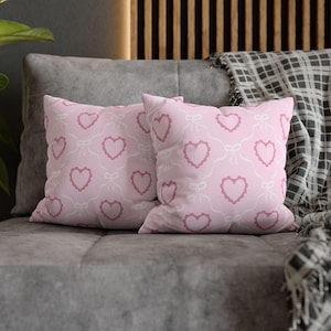 May include: Two square throw pillows featuring a repeating pattern of dark pink hearts with scalloped edges on a light pink background. The hearts are connected by thin white line drawings of bows and ribbons, creating a continuous grid design.