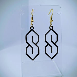 May include: A pair of black geometric earrings in the shape of the "S" symbol, with gold-coloured fish hook ear wires. The earrings are displayed on a clear acrylic stand against a light background.