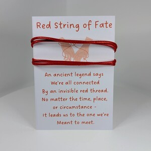 May include: A white card with the text "Red string of Fate" and a poem about connection. Two strands of red string are wrapped around the card. The card features a drawing of two hands holding each other.