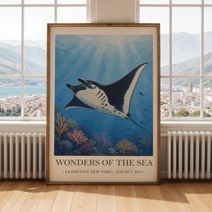 Può includere: Una stampa artistica incorniciata con una manta che nuota in un oceano blu. L'opera d'arte ha uno stile vintage, con il testo "Wonders of the Sea" e i dettagli della mostra in basso. La manta è nera e bianca.