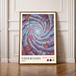 Puede incluir: Una impresión artística enmarcada con un diseño en espiral abstracto y colorido con patrones florales y de puntos. La obra de arte, de Yayoi Kusama, incluye texto en inglés y japonés, con una ubicación en Tokio. La paleta de colores incluye azules, morados, rosas y verdes.