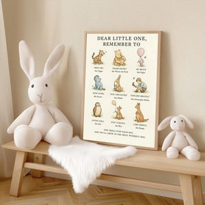 May include: A framed print with Winnie the Pooh characters and the text "DEAR LITTLE ONE, REMEMBER TO." Two white plush bunny toys and a white faux fur rug sit on a light wood bench. The print features illustrations and inspirational phrases.