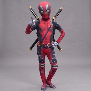 Op de afbeelding: Een rood en zwart spandex kostuum voor het hele lichaam met een bijpassend masker met witte oogstukken. Het pak bevat een bedrukte riem, opbergzakjes en een diagonale band. Twee zwart-gouden katana's zijn op de rug van het pak bevestigd.