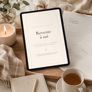 May include: A tablet displaying a digital document titled Revenir à soi with French text, positioned on a wooden tray alongside printed pages, a lit candle in a white holder, a beige notebook with a gold pen, and a plaid fabric cloth.