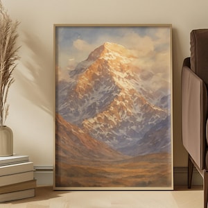 Puede incluir: Una pintura de acuarela enmarcada de una cordillera nevada. La obra presenta una paleta de colores cálidos con tonos dorados y marrones en primer plano y una cima brillante e iluminada por el sol. La pintura se exhibe en una pared de color claro.