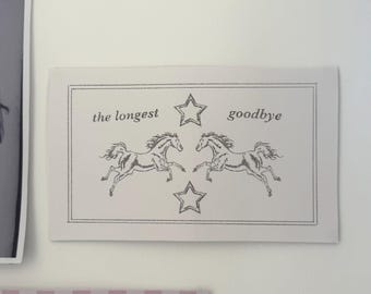 May include: A rectangular print with the words "the longest goodbye" and two running horses. The print is bordered with a dotted line and includes three star illustrations. The print is in black and white.