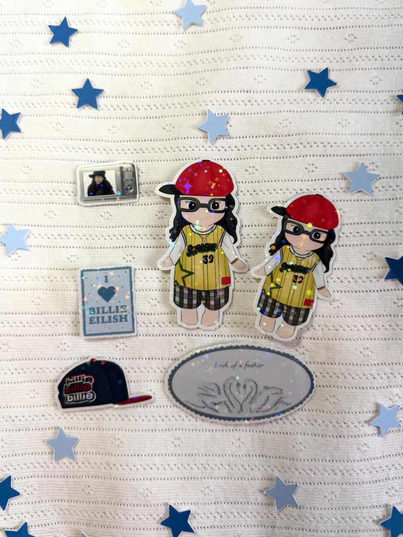 May include: A collection of stickers and a baseball cap featuring a cartoon girl wearing glasses and a red hat. The stickers include a small TV, a heart-shaped design with the text "Billie Eilish", and an oval sticker with the text "birds of a feather".