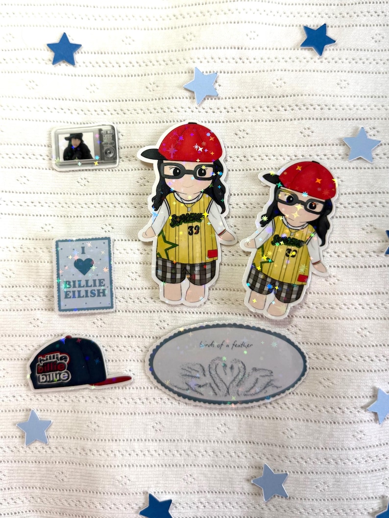 May include: A collection of stickers and pins featuring a cartoon character wearing a red baseball cap and glasses, a blue baseball cap, a television, and the text "Billie Eilish". The stickers are surrounded by blue stars.
