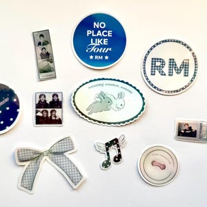 May include: A selection of stickers featuring diverse designs. Includes a blue circular sticker with the text "NO PLACE LIKE TOUR" and "RM" stars, a sticker with "RM" in a checkered pattern, and stickers with photo booth style images.
