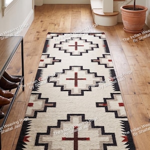 Puede incluir: Alfombra de pasillo color crema con un patrón geométrico en negro, gris y rojo. La alfombra presenta un diseño de cruz central y un borde con un patrón repetitivo. La alfombra se exhibe sobre un suelo de madera en un pasillo.