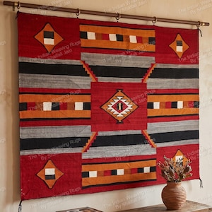 May include: A rectangular woven wall hanging featuring a geometric pattern in red, black, grey, orange, and white. The textile displays a central diamond motif, horizontal bands, and smaller diamonds in the corners, suspended from a dark metal rod.