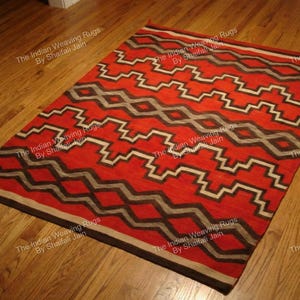 Può includere: Un tappeto rettangolare rosso con un motivo geometrico a zig-zag bianco, nero e grigio. Il tappeto è posizionato su un pavimento in legno. Il tappeto ha un bordo marrone scuro.