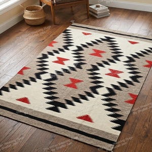 Può includere: Tappeto rettangolare con motivo geometrico in nero, rosso e beige. Il tappeto presenta un disegno centrale di forme a diamante bianche e nere con accenti rossi. Il bordo è una striscia nera piena. Le nappe sono visibili su un'estremità.