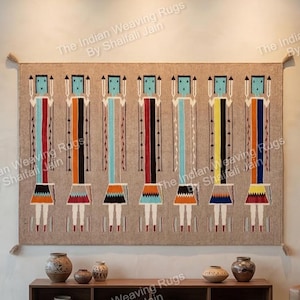 Puede incluir: Un gran tapiz rectangular tejido con siete figuras estilizadas con diseños verticales coloridos. Cada figura tiene un cuerpo beige, una falda estampada y una cabeza con la parte superior cuadrada. La obra de arte se exhibe en un salón moderno.