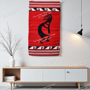 Op de afbeelding: Een rode geweven wandkleed met een zwarte Kokopelli-figuur in het midden. Het kleed heeft zwart-witte geometrische patronen aan de boven- en onderkant, met de tekst "The Indian Weaving Rugs By Shaifali Jain" herhaald.