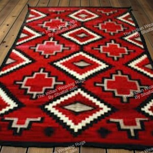 Può includere: Un tappeto rettangolare rosso con un motivo geometrico di forme bianche, nere e beige. Il tappeto presenta disegni a forma di diamante e croce. Il tappeto è posto su un pavimento in legno.