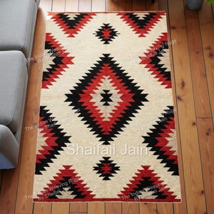 Può includere: Tappeto rettangolare color crema con un motivo geometrico rosso e nero. Il design presenta forme a diamante e a zig-zag. Il tappeto è su un pavimento in legno.