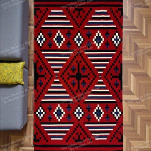 Può includere: Un tappeto rettangolare rosso con un motivo geometrico. Il design presenta forme a diamante, strisce e croci in nero, bianco e blu. Il tappeto è posizionato su un pavimento in legno, con un divano grigio e un cuscino giallo visibili.