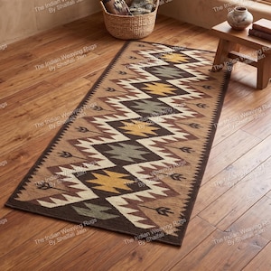 Peut inclure: Un tapis rectangulaire à motifs géométriques dans les tons marron, beige, jaune et gris. Le motif présente des losanges et des flèches. Le tapis mesure environ 150 cm de long et est posé sur un sol en bois.