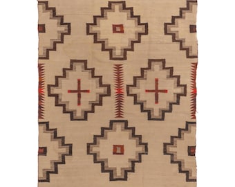 Op de afbeelding: Een rechthoekig, beige tapijt met een geometrisch patroon. Het ontwerp bevat herhalende ruitvormen in bruin- en grijstinten, met rode kruis- en vierkante accenten. Het tapijt heeft een gefranjerde rand.