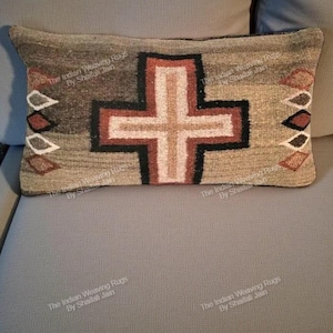 Puede incluir: Cojín rectangular con un diseño de cruz. La cruz central es de color marrón, negro y crema, sobre un fondo neutro. Los lados están adornados con formas de diamantes decorativos de varios colores.