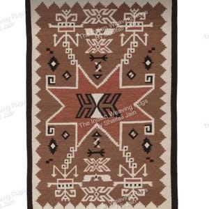 Può includere: Un tappeto rettangolare tessuto con un motivo geometrico nelle tonalità del marrone, crema e nero. Il disegno centrale presenta una forma a stella con dettagli intricati. Il tappeto ha un bordo nero e il testo "The Indian Weaving Rugs By Shaifali Jain" è visibile.